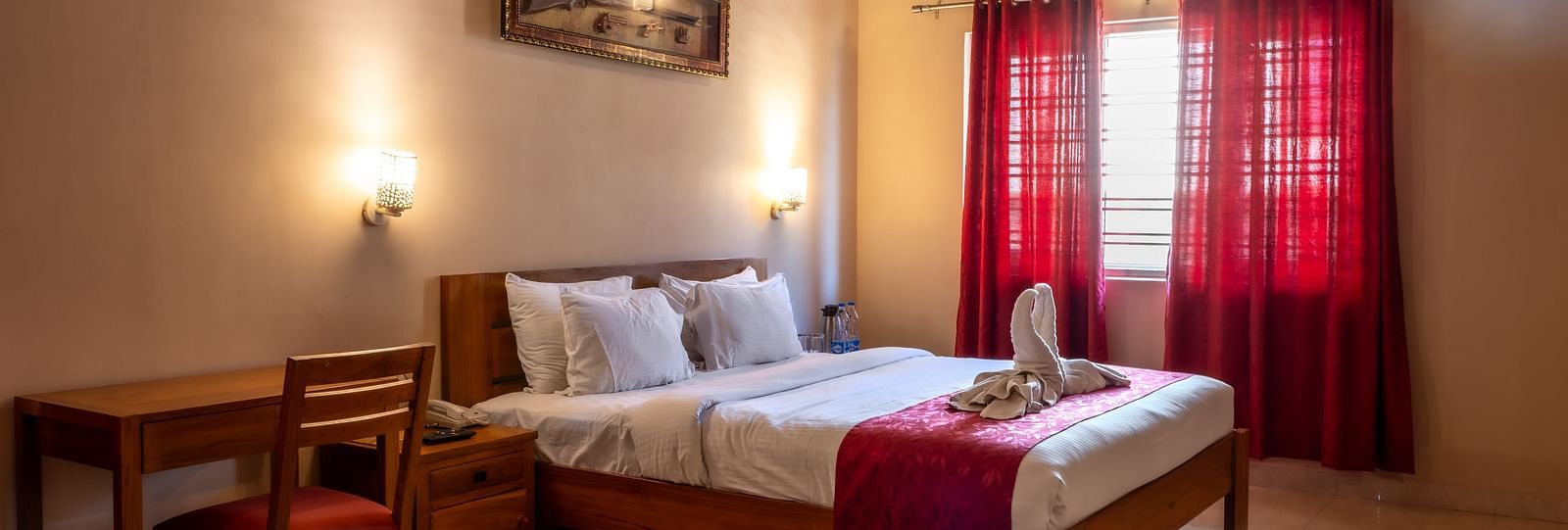 Attic Villa includes a wooden bed with white linens, red curtains, a writing desk, and wall-mounted artwork | Woodstock Resorts, Coorg