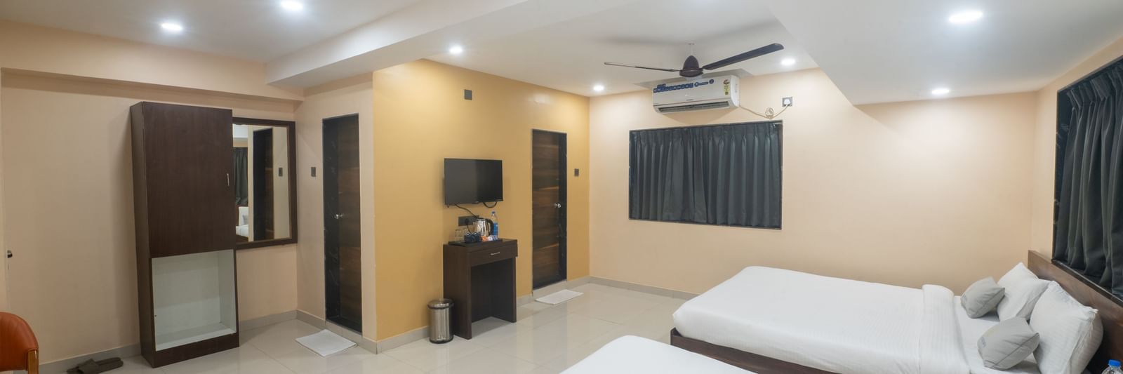 A spacious room at Pravasa Stay, Shirdi, contains two beds, a wardrobe, and a television on a small desk.