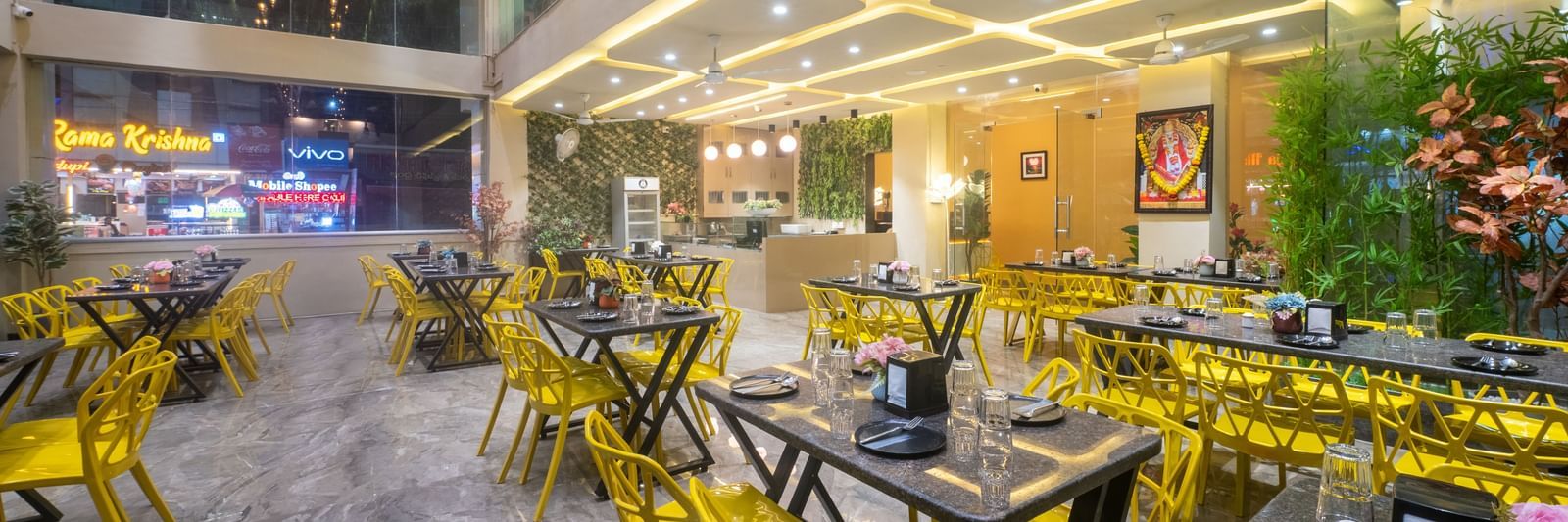 The dining space at Pravasa Stay, Shirdi, features bright yellow chairs and many ceiling lights.