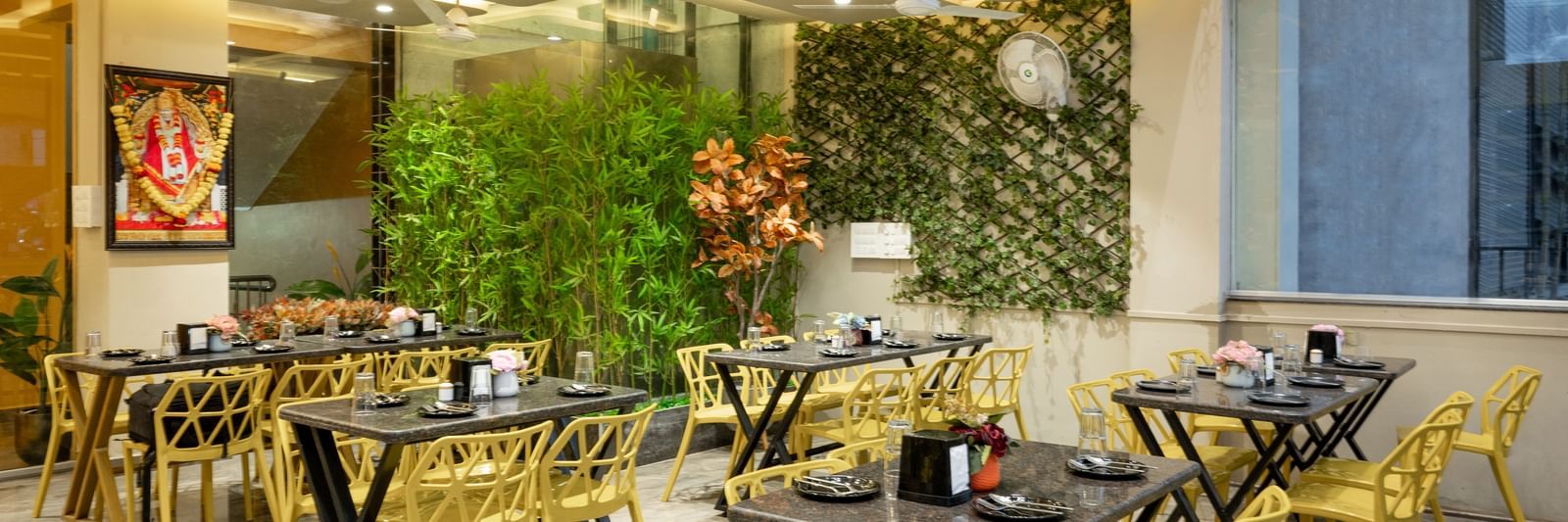 The restaurant at Pravasa Stay, Shirdi, has yellow chairs, black tables, and decorative green walls.