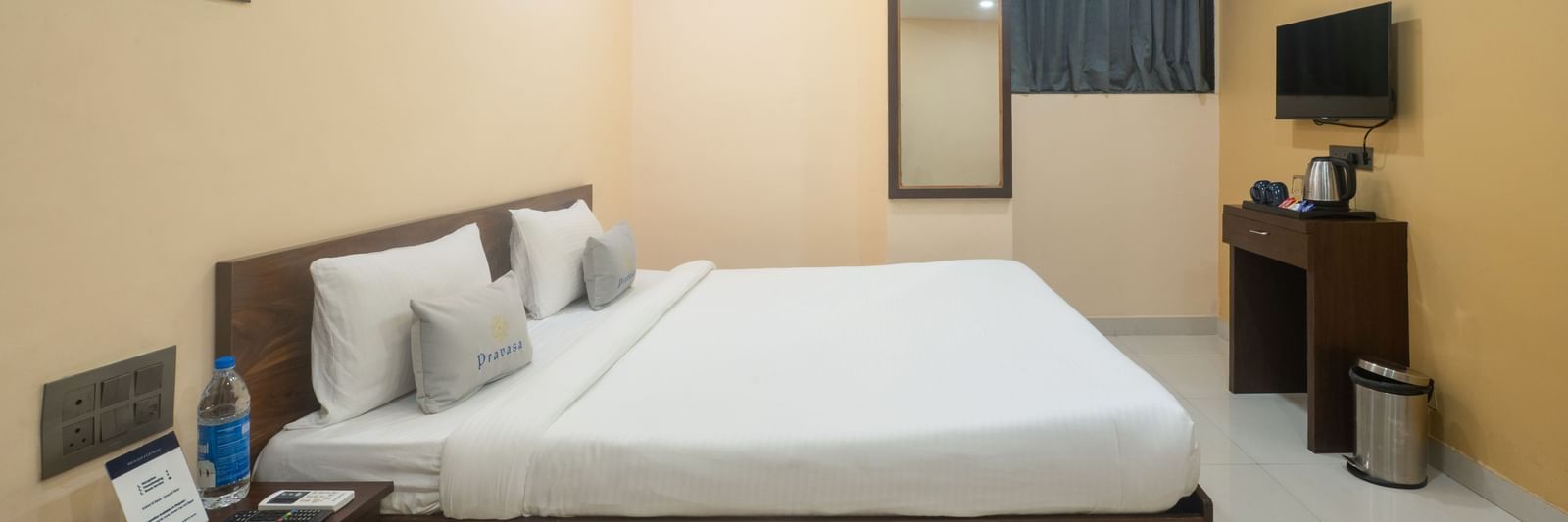 This room at Pravasa Stay, Shirdi, features a large wooden bed frame, a mirror, and a television on the opposite wall.