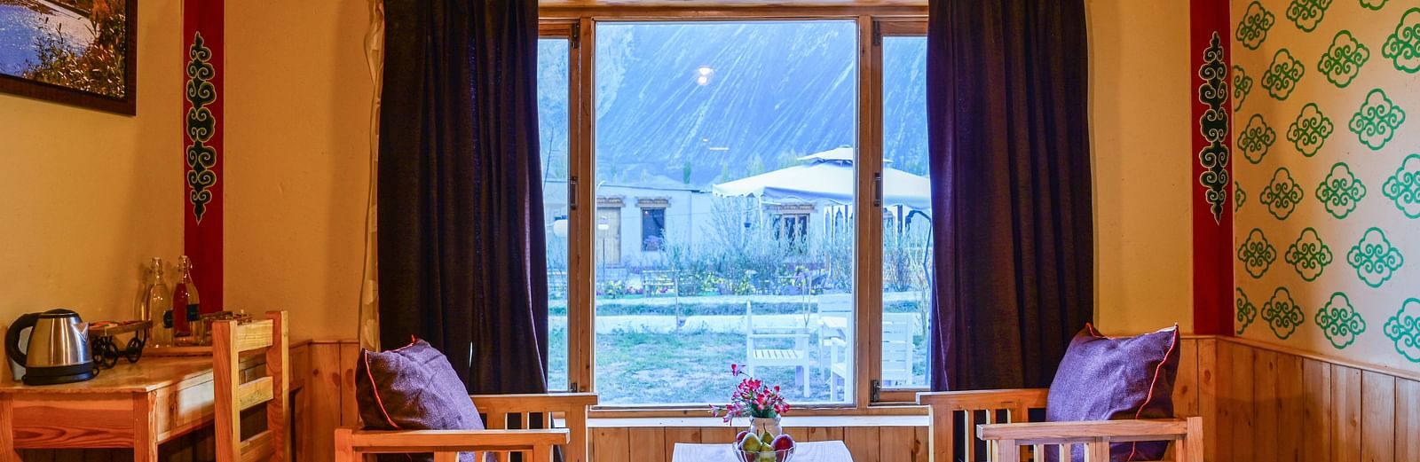 Premium Cottage at White Sands Resort, Ladakh, is furnished with a king size bed, a dining table, chairs, and vibrant wallpaper.