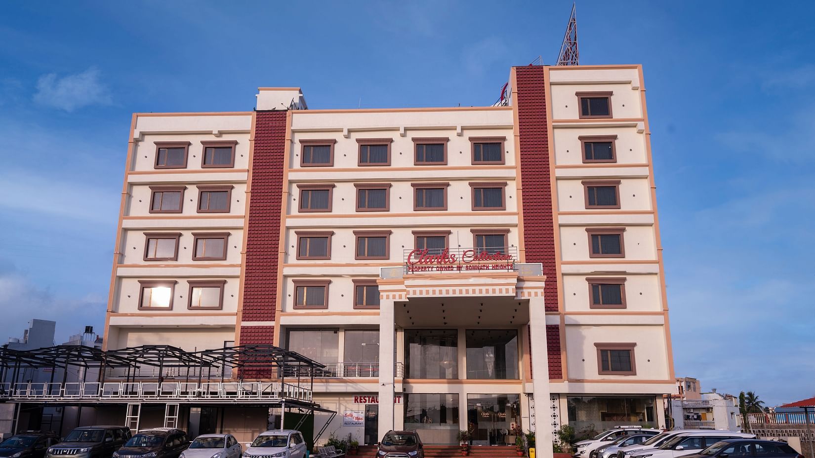 Front view of Clarks Collection Somnath building with facade, multiple floors, parked cars, and a clear blue sky background.