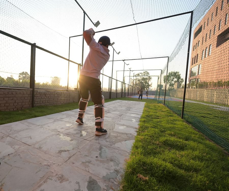 Two men playing cricket on a makeshift pitch, wearing cricket gear during the golden hour - Clarks Safari, Haridwar