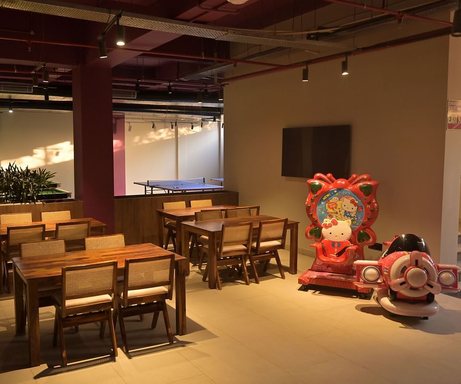 Three sets of chairs and tables arranged in a room, next to a huge Hello Kitty throne and a toy aeroplane for babies, with indoor plants and a ping pong table in the background - Clarks Safari, Haridwar
