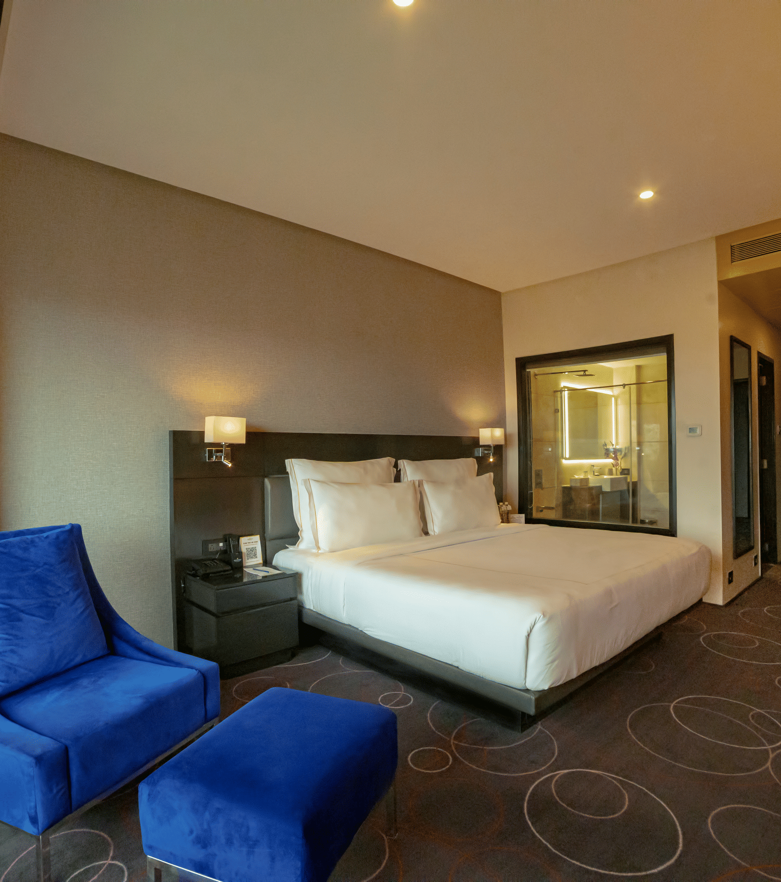 Hotel room featuring a double bed and a blue lounge chair with a leg rest – Narayani Heights Hotel & Resorts