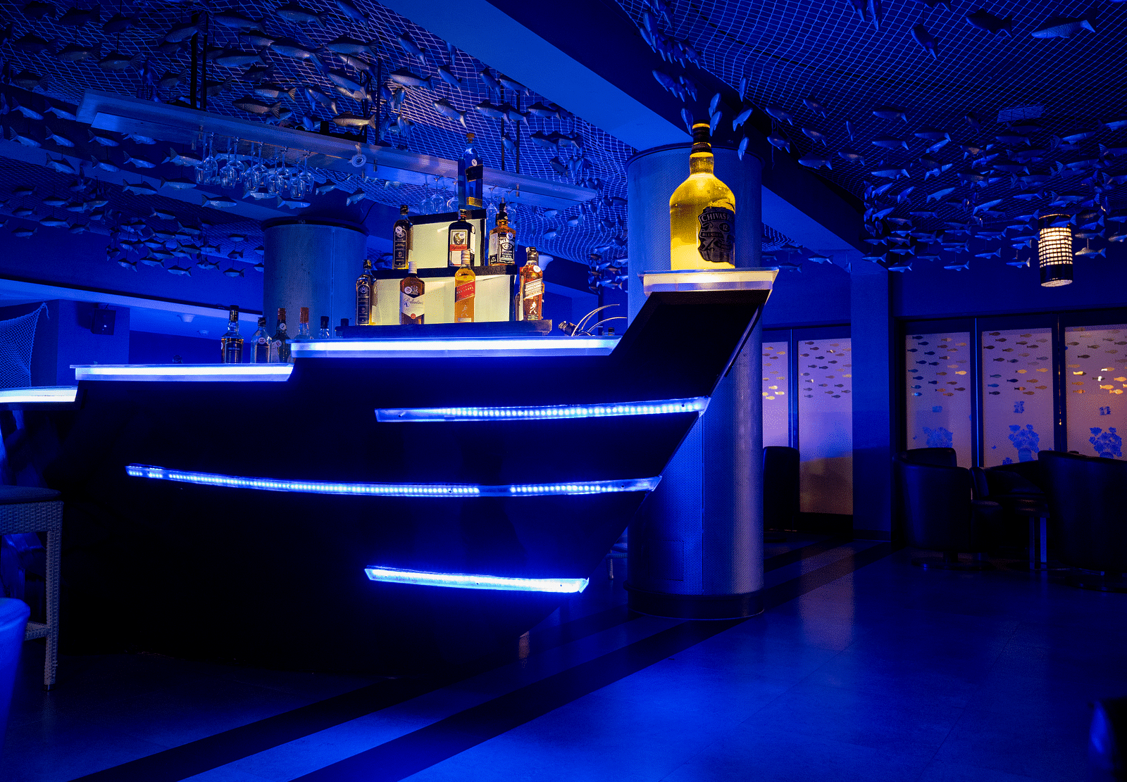 An image of ship themed bar with different varieties of liquor  bottles at image of an event hall with tables and chairs at Grand Kakinada by GRT Hotels