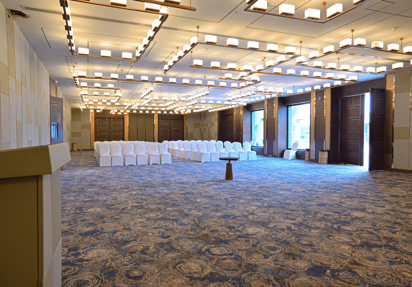 A large, empty event hall with a patterned carpet, modern lighting, and chairs set up for a gathering.