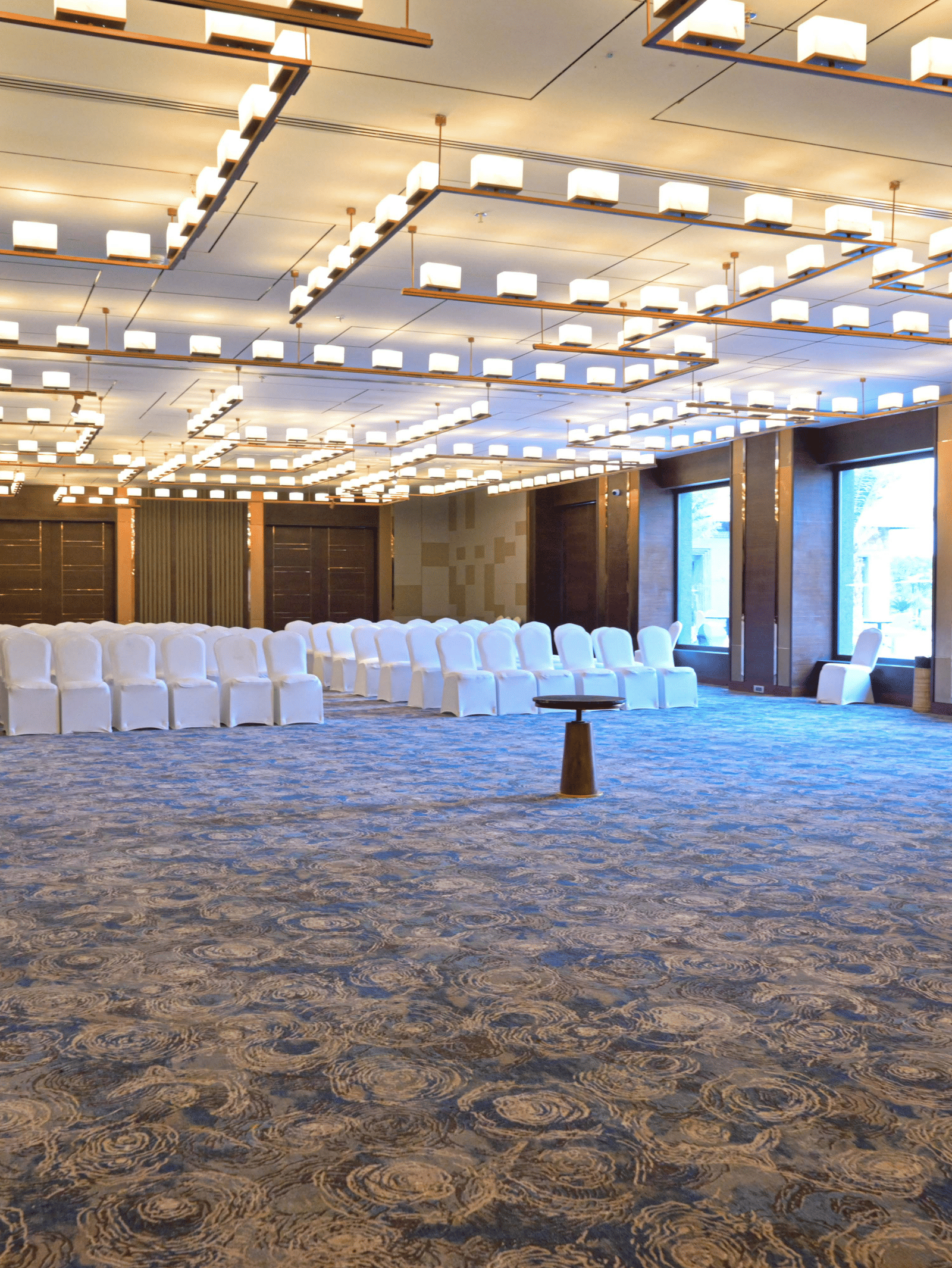 A large, empty event hall with a patterned carpet, modern lighting, and chairs set up for a gathering.