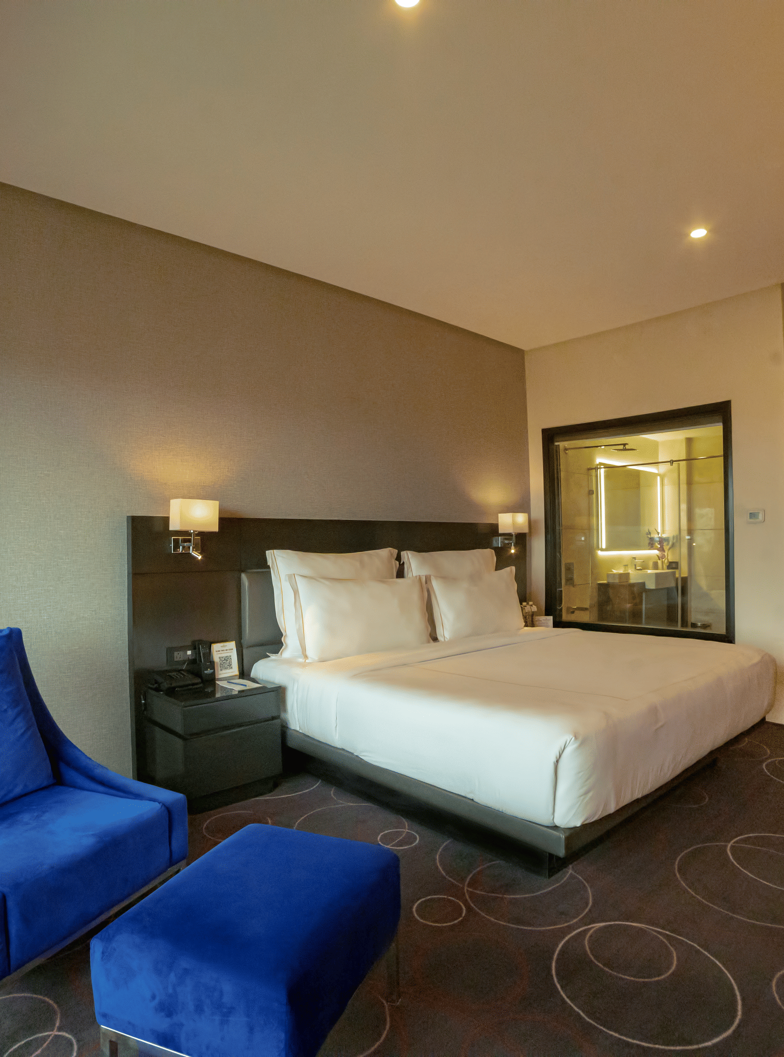 Hotel room featuring a double bed and a blue lounge chair with a leg rest – Narayani Heights Hotel & Resorts