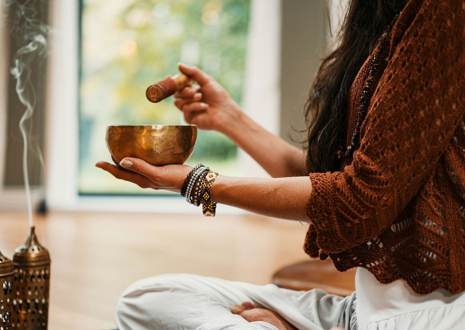 A close up shot of a woman using a bowl and a stick for meditation with an incense stick in front of her.
