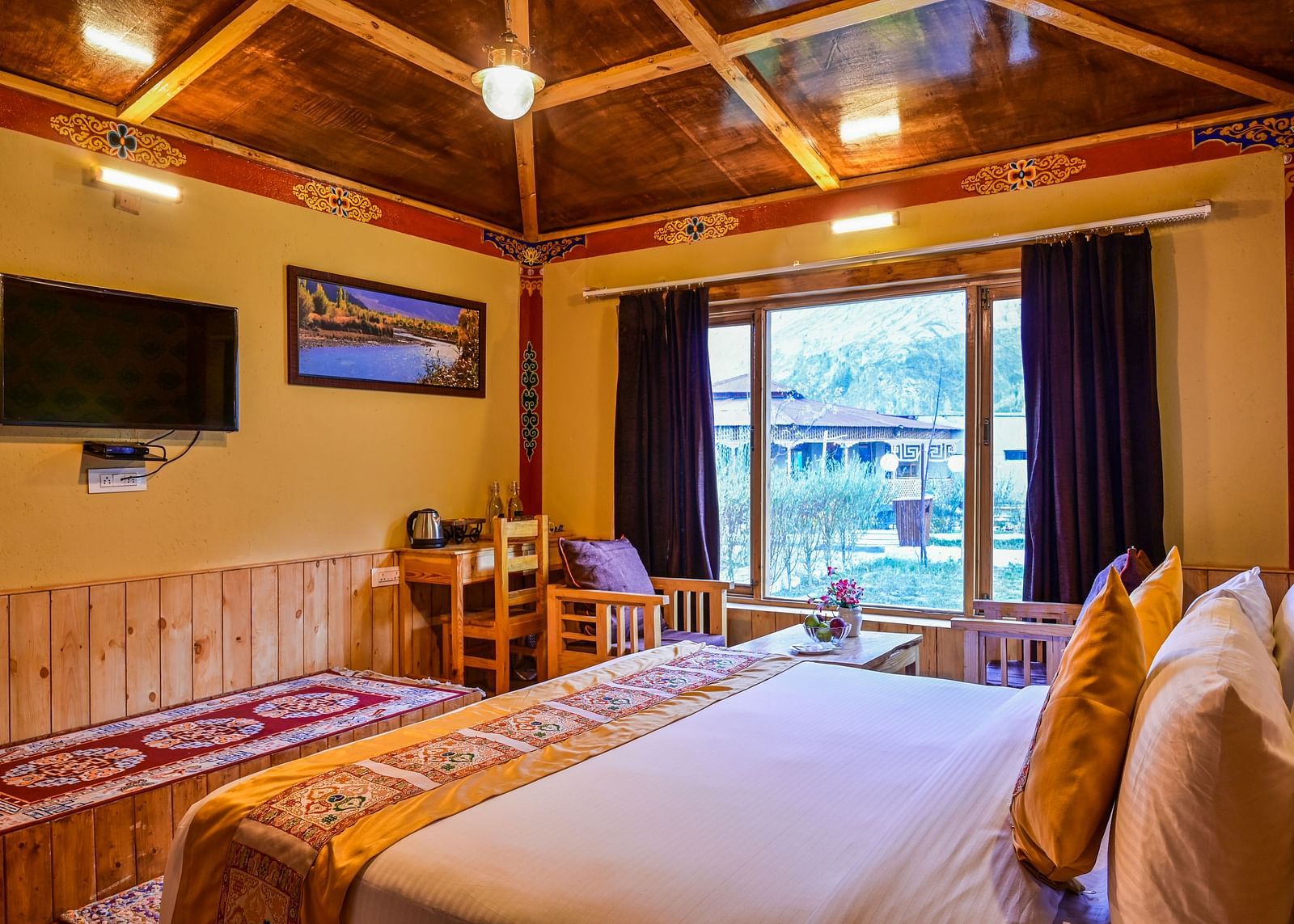Premium Cottage at White Sands Resort, Ladakh features a king size bed with patterned linens, a seating area, and a view of the outdoors through a window.