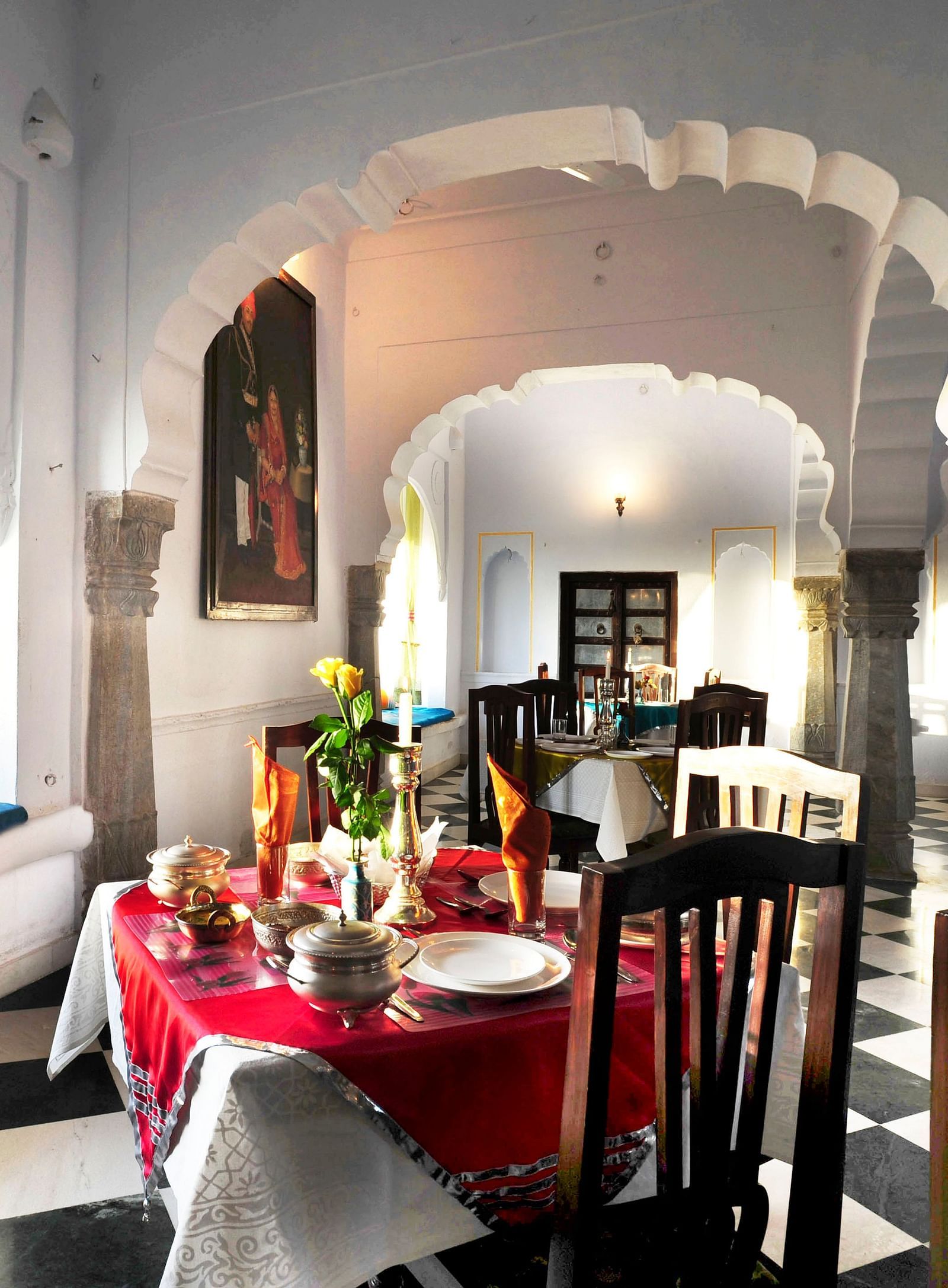 A bright dining area at Fort Barli, featuring arched doorways, checkered floors, and a window seat, blends architectural charm with a cosy meal setting.