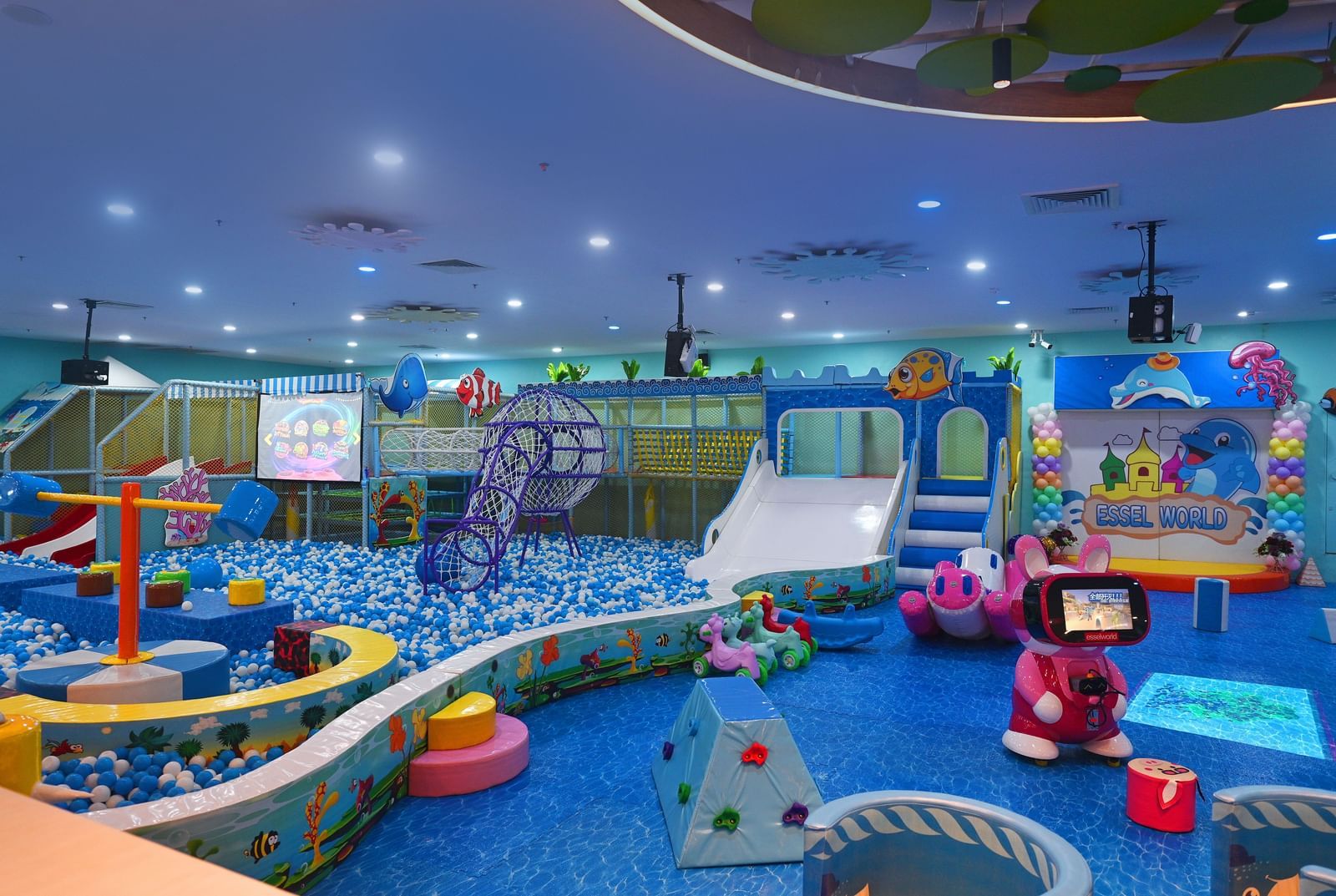 Indoor playground with colorful equipment, slides, and a ball pit, filled with children playing.
