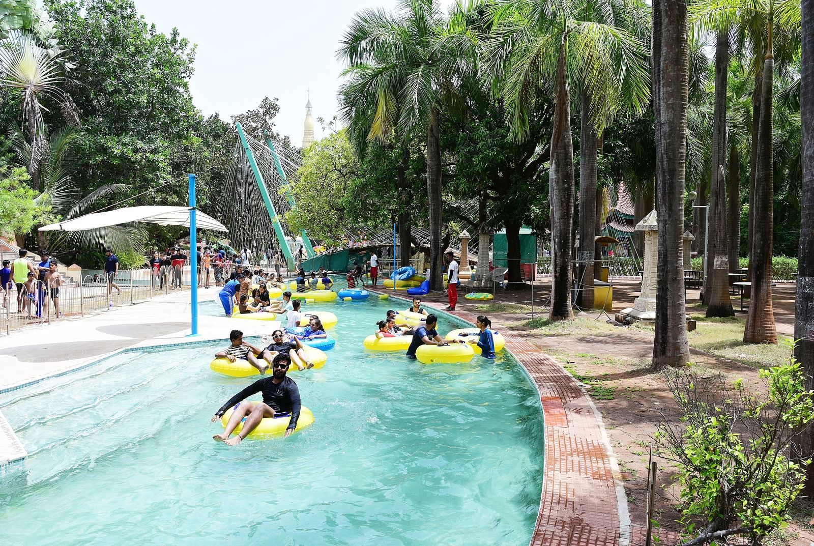 People enjoy a lazy river ride in a water park, surrounded by palm trees and greenery.