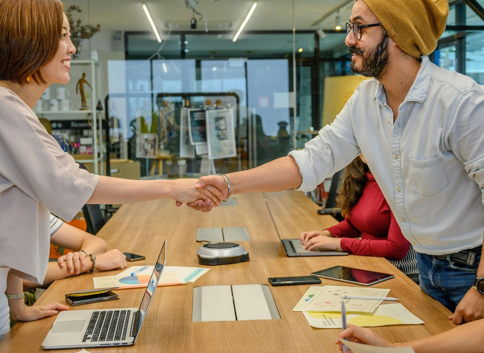 Two colleagues in an office setting shaking hands over a conference table.