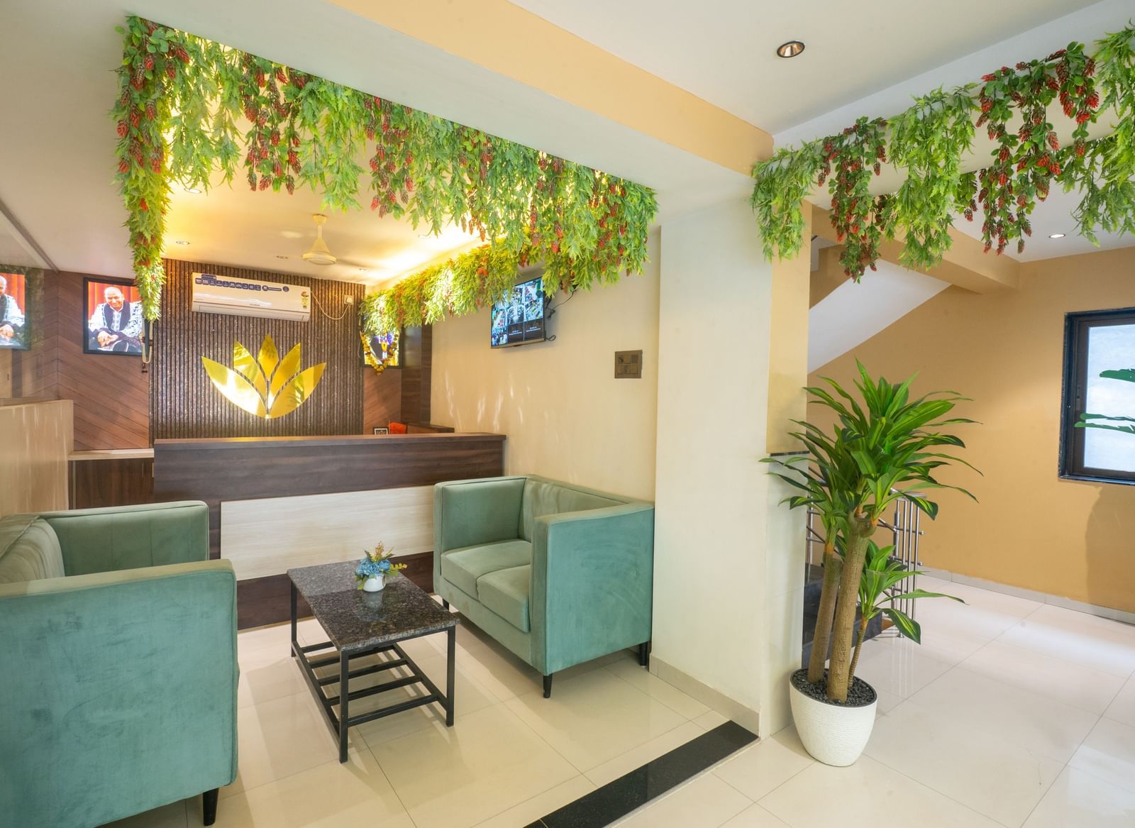 The reception area of Pravasa Stay, Shirdi, has two cushioned chairs and a desk adorned with a gold emblem.