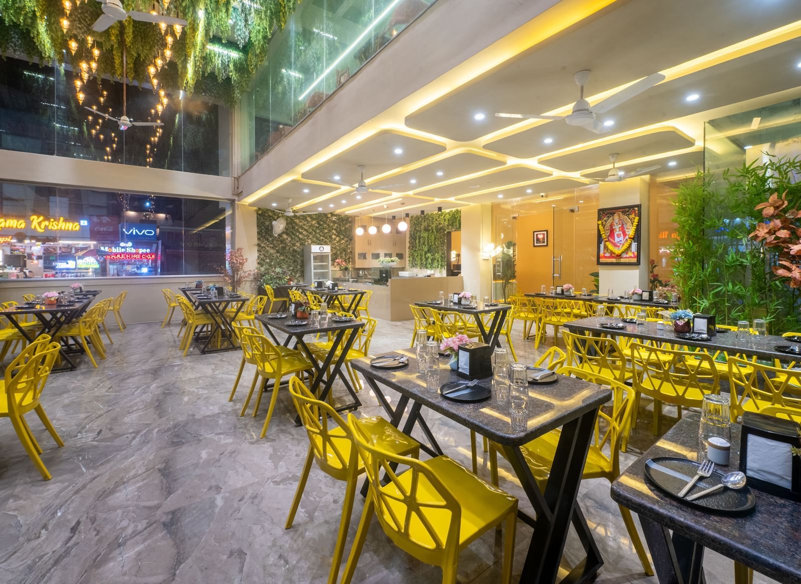 The dining space at Pravasa Stay, Shirdi, features bright yellow chairs and many ceiling lights.
