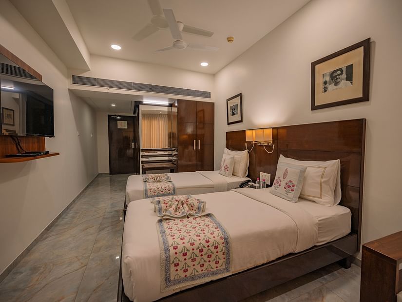Room with two single beds, TV, wooden wardrobe, and framed photos at Clarks Collection Vadodara.
