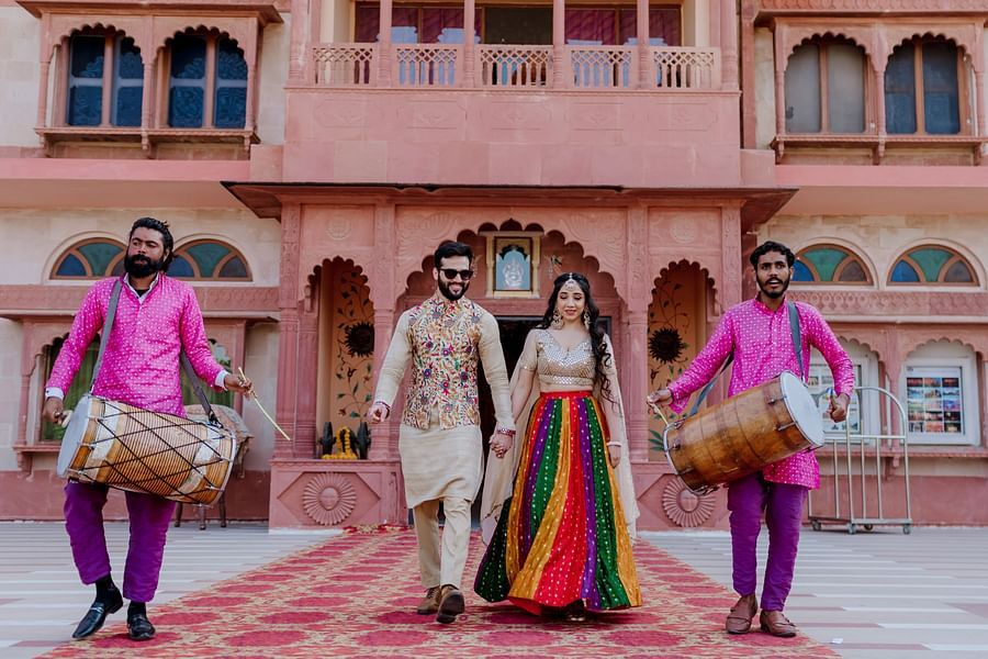  A couple walks hand in hand, with drummers in colourful outfits accompanying them at Umaid Palace - Best Luxury Heritage Resort Near Jaipur 