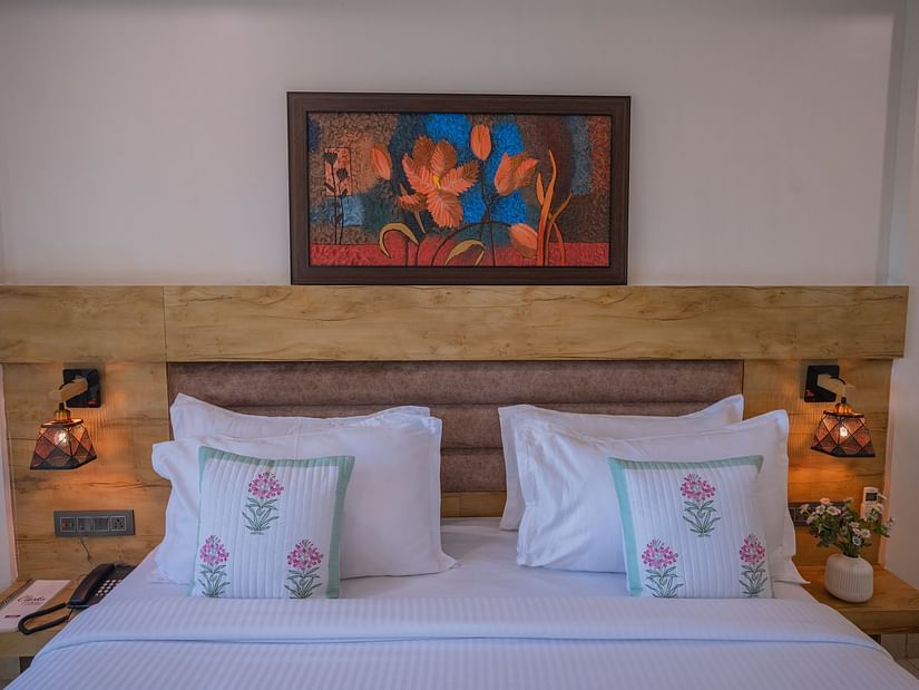 The front view of a double bed with floral pillows, lamps, and wall art above at Clarks Collection, Somnath.