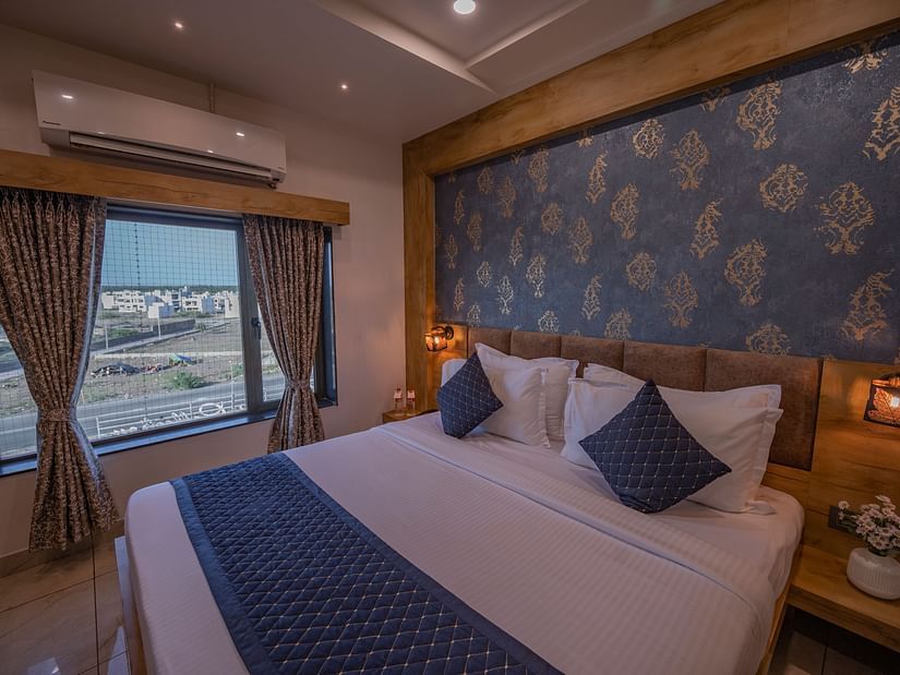 Spacious room with a double bed, ac, water bottles, bedside table with flower vase on the top and city view window at Clarks Collection, Somnath.