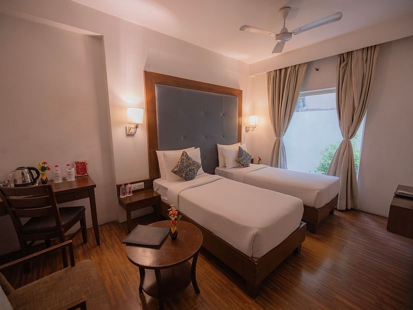 Warmly lit bedroom at Clarks Collection Bhavnagar with twin bed, desk, and chairs.