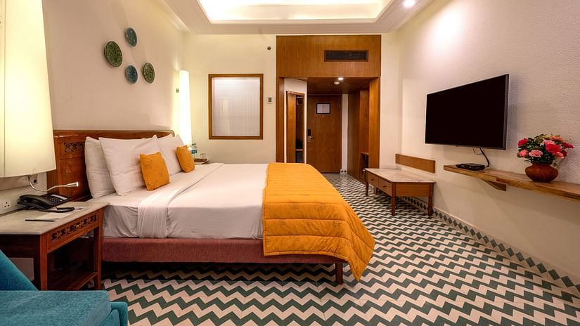 A well-lit hotel room with a king-size bed, a blue sofa, and a flat-screen TV at Clarks Amer, Jaipur.