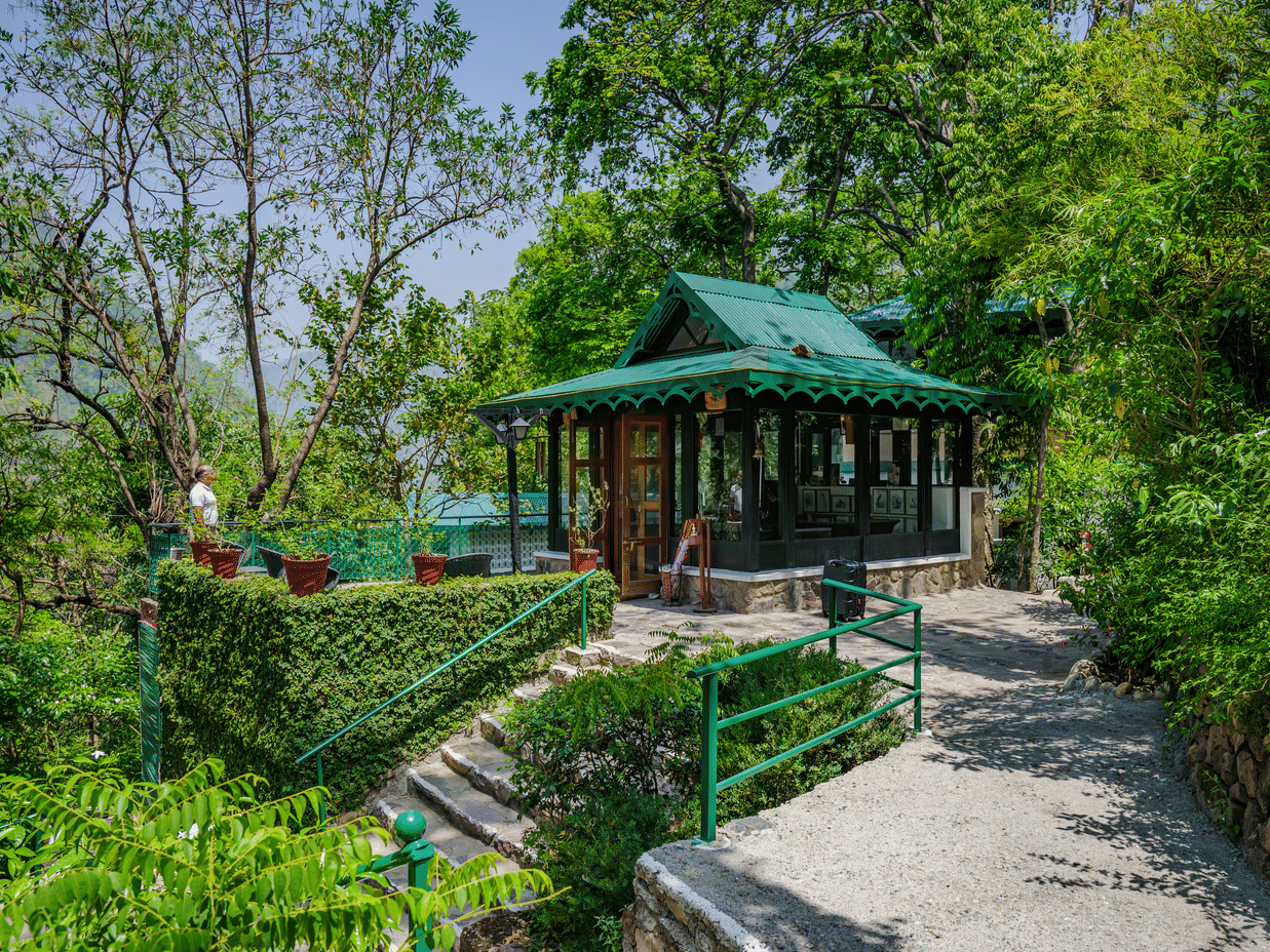 A roofed area surrounded by lush greenery and paved pathways at Neemrana's Glasshouse on The Ganges.