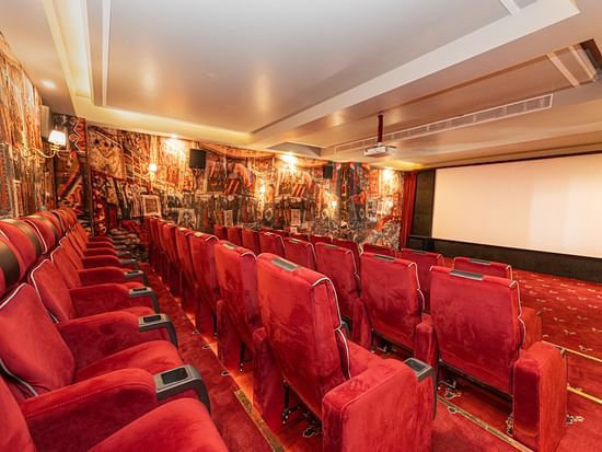 Luxurious private cinema with plush red velvet seating, ornate carpet décor, and projection screen at The Manor Wellness & Sports Hotel