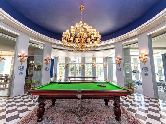 Elegant game room at The Manor Wellness & Sports Hotel - stunning blue ceiling, golden chandelier & professional snooker table in grand circular space.