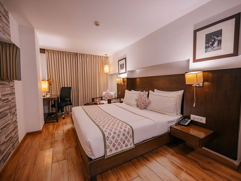 Wide view of the room showing the bed, armchair, lamps, curtains, and work desk with chair at Clarks Collection, Vadodara.
