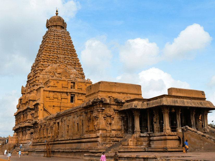 A facade view of Brihadeeswarar Temple in Thanjavur in all its glory with people walking next to it and blue sky in the background, as seen during the summer in Thanjavur.
