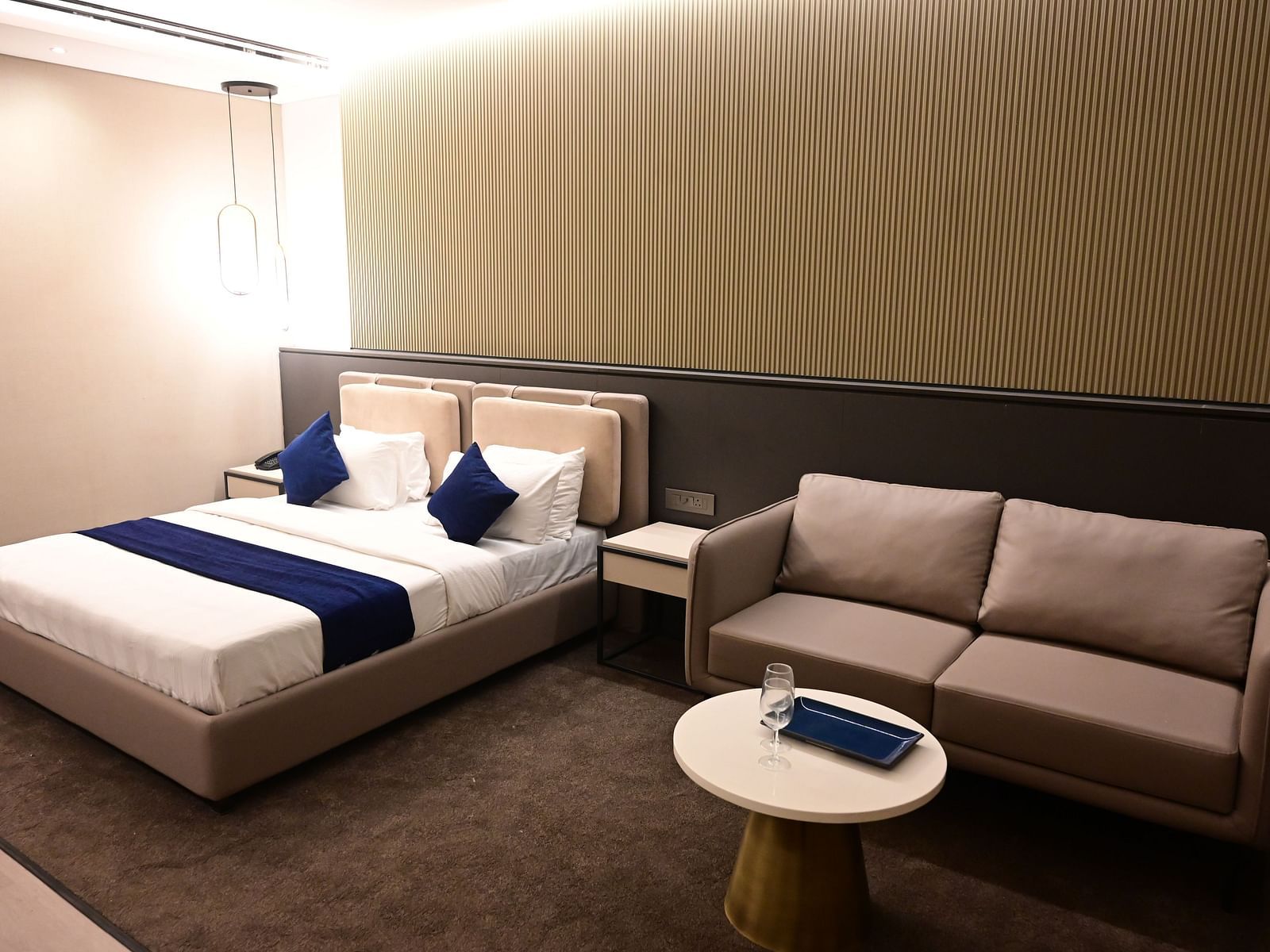 corner view image of the imperial guest suite featuring a double bed and a couch with a coffee table i front of it at club charholi, pune