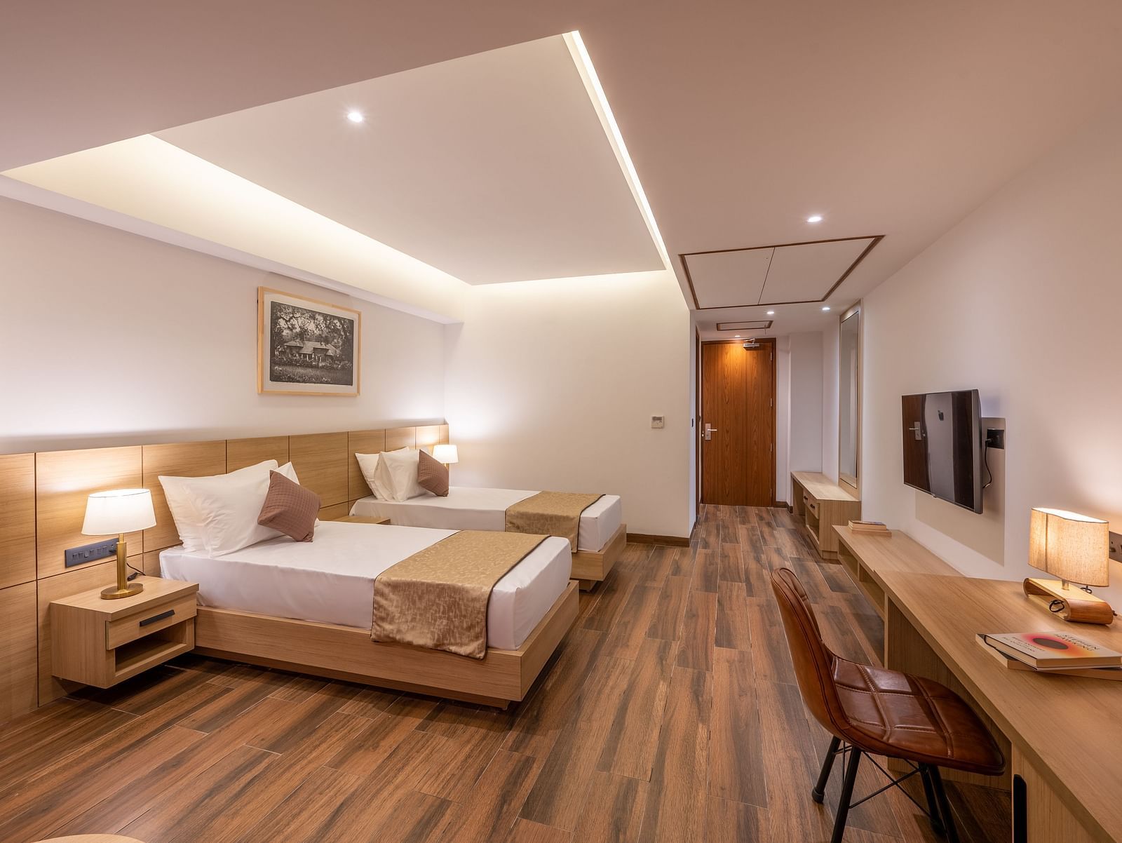 Side shot of Twin Room at Vishranti Hotel, Dehradun featuring twin beds, side table with bed lamp and a work desk.