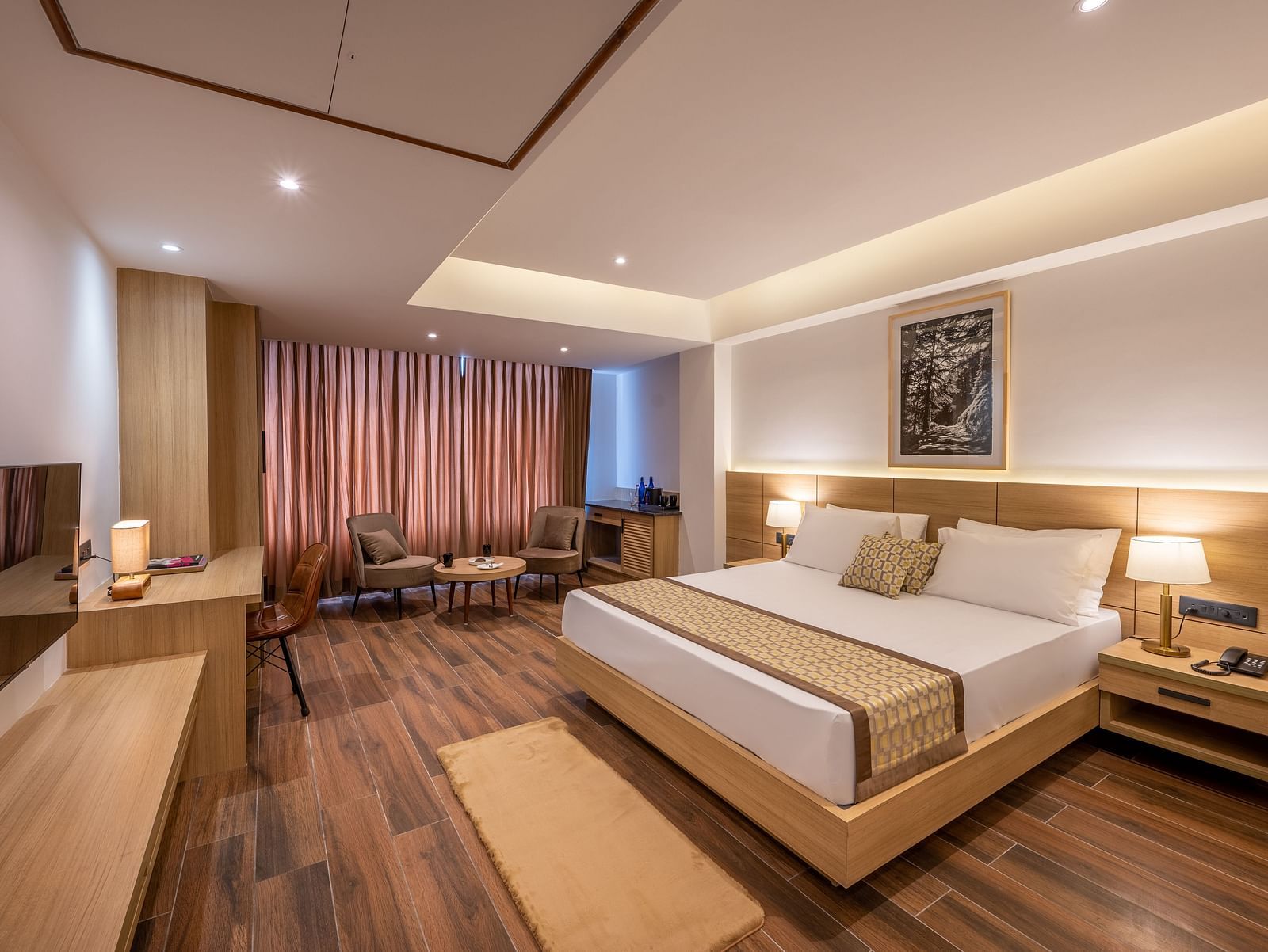 Full shot of Suite at Vishranti Hotel, Dehradun featuring a king bed with side tables, a TV, large window with curtains and bed lamps. 