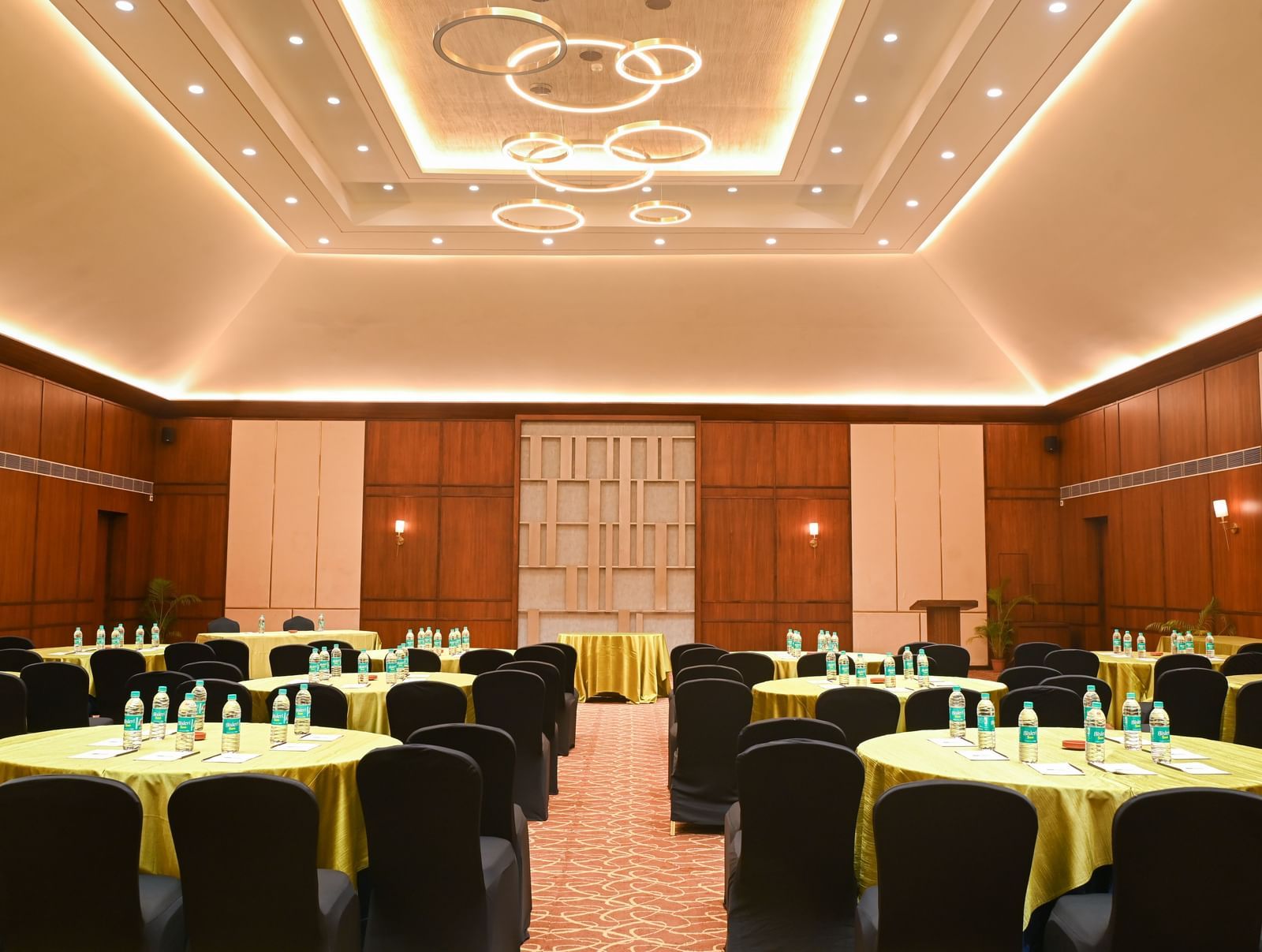 Om Ballroom in Vedic Village Spa Resort, featuring a neat space with round tables, black chairs, gold linens, and a podium.