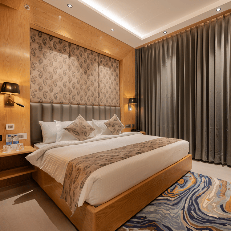 A bright guest room featuring a king-sized bed with a patterned headboard and floor-to-ceiling grey curtains at Ananta Express, Katra.