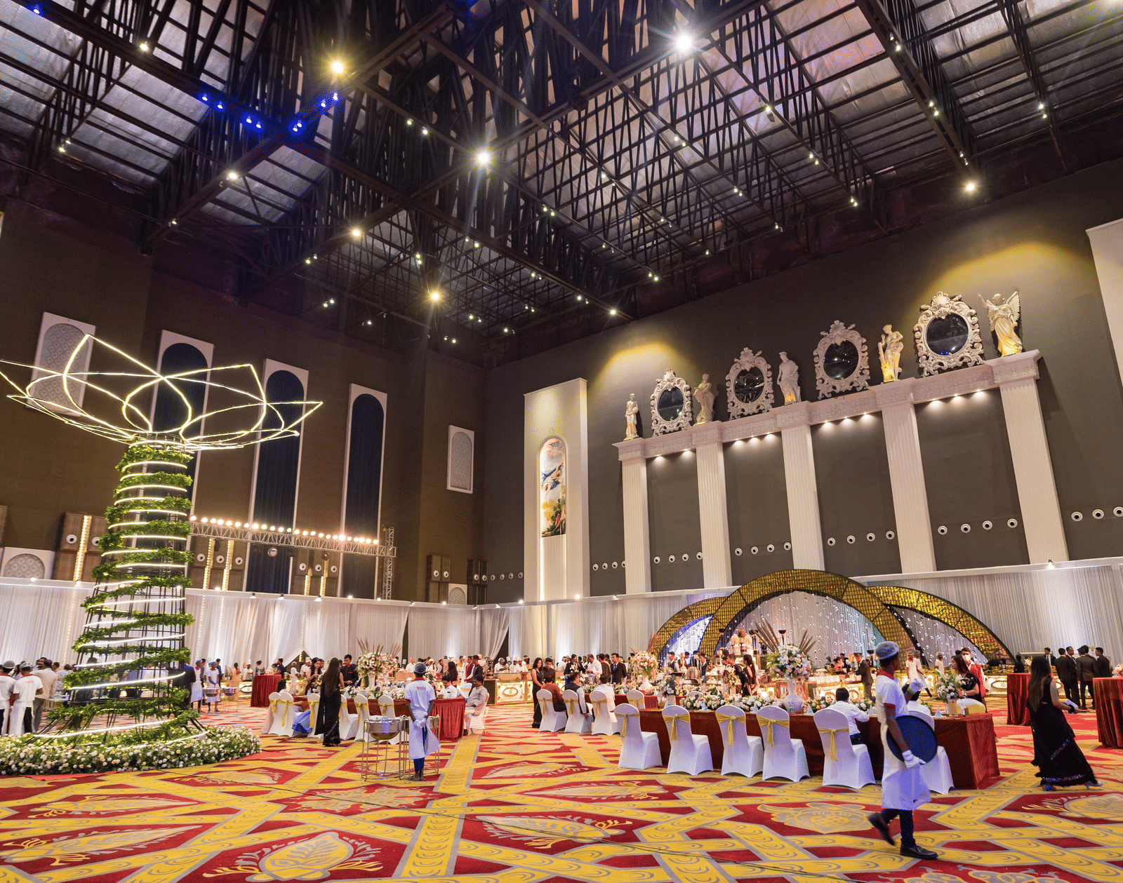 Vast, high-ceilinged convention or banquet hall decorated for an event with a large hanging ornament and a crowd of people at Hotel Hukam's Lalit Mahal.