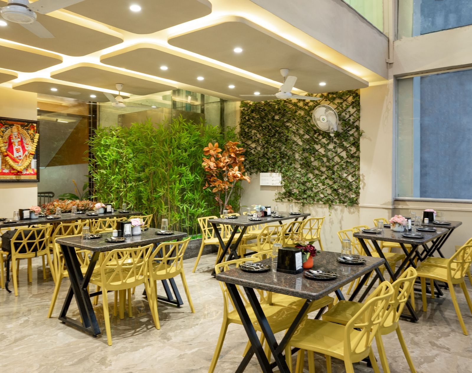 The restaurant at Pravasa Stay, Shirdi, has yellow chairs, black tables, and decorative green walls.