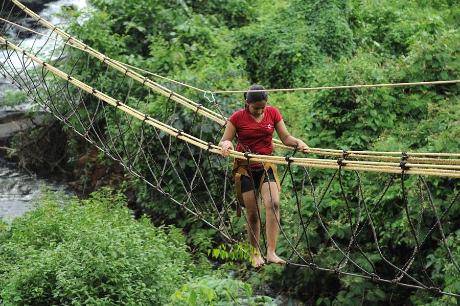 alt-text A focused individual crossing a rope bridge over a lush, green area. They appear determined, showcasing an adventurous outdoor activity.
