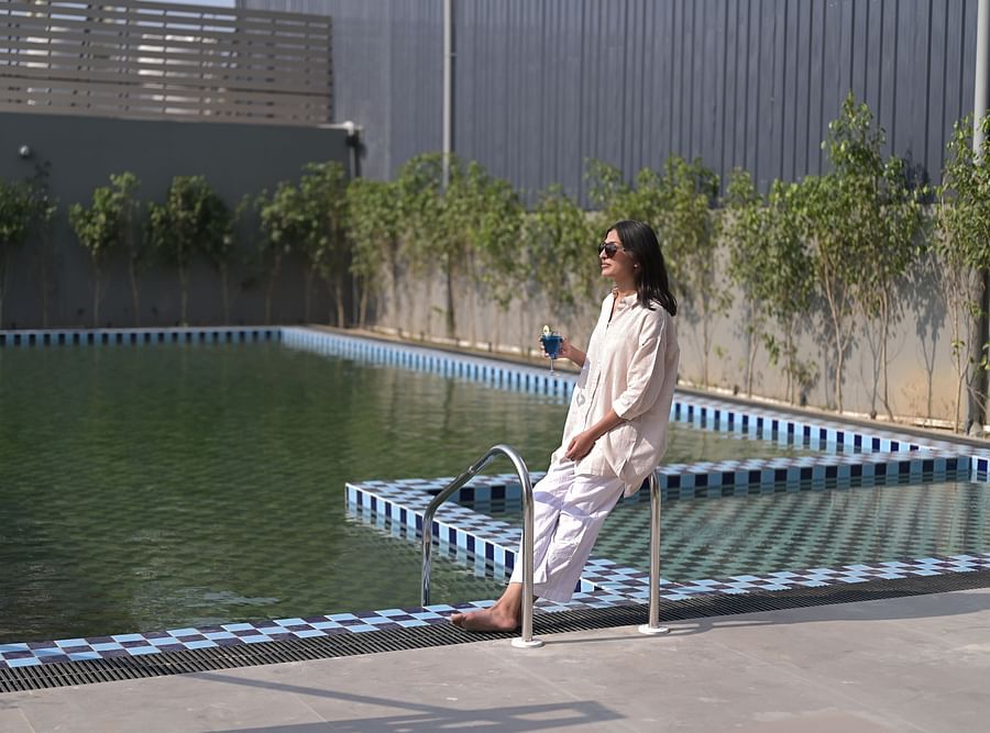 A woman holding a drink in her hand standing at the corner of a swimming pool on a bright sunny day. - Clarks Safari Haridwar