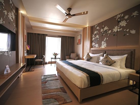 A bedroom with partially opened curtains allowing natural light to fill the room, at Clarks Collection Grand Sapphire, Ajmer.