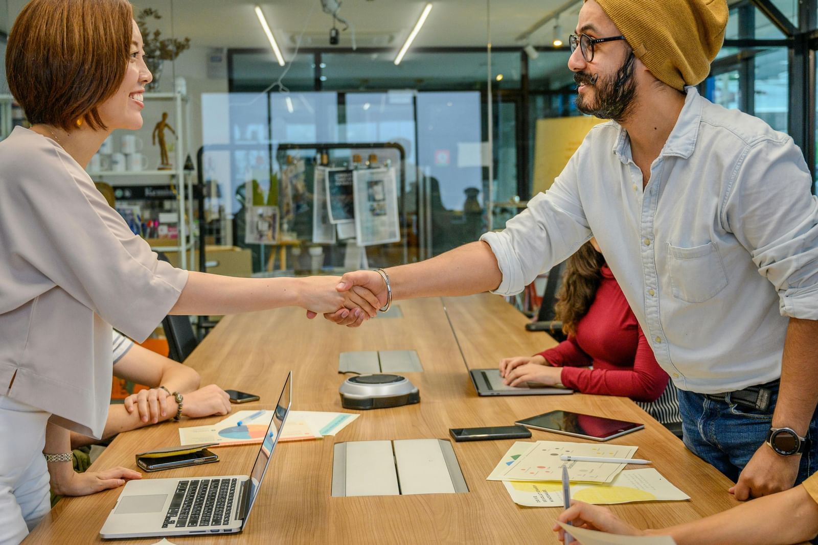 Two colleagues in an office setting shaking hands over a conference table.