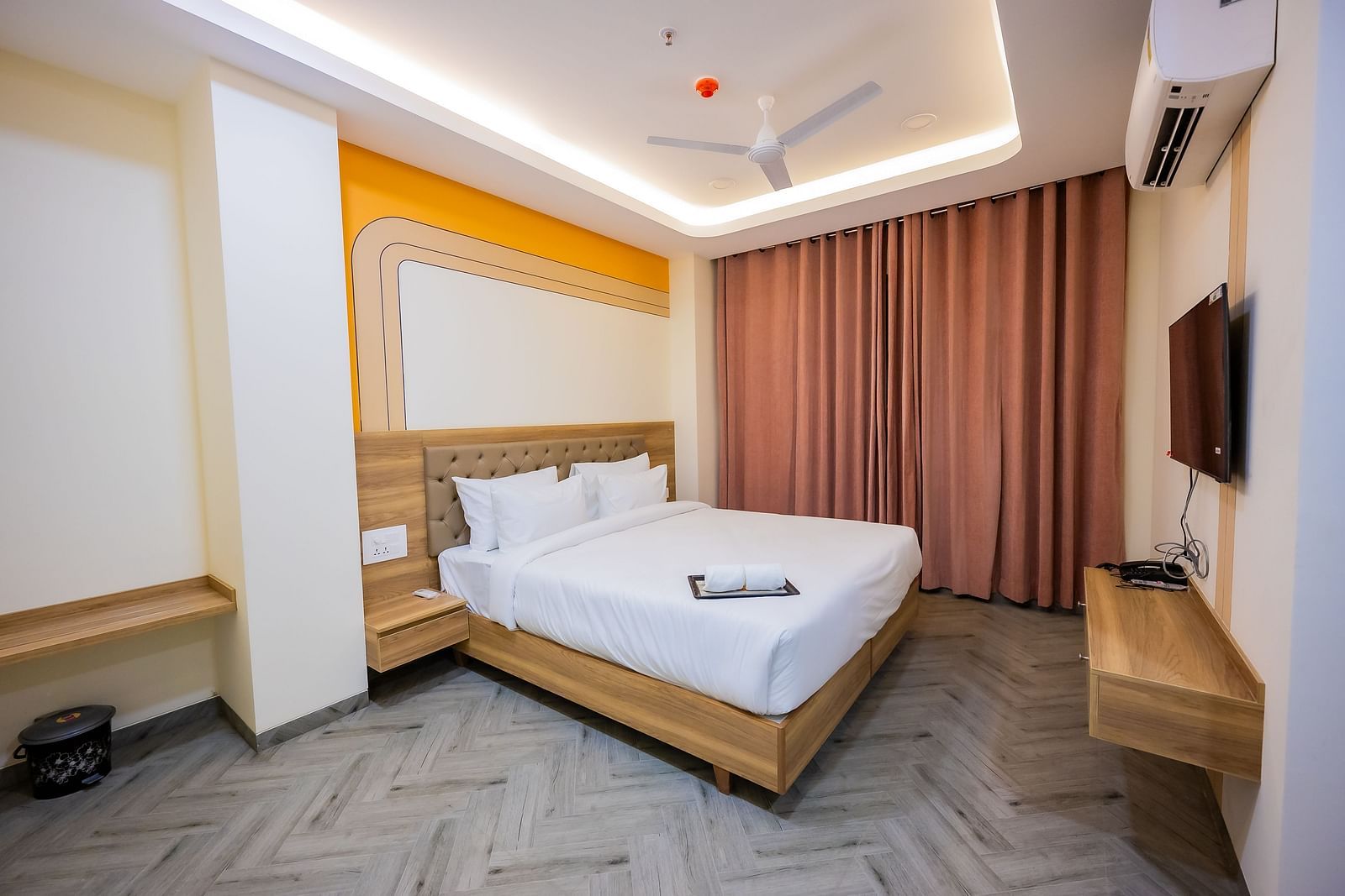 A cosy hotel room with soft lighting, a bed, curtains, and a TV mounted on the wall.
