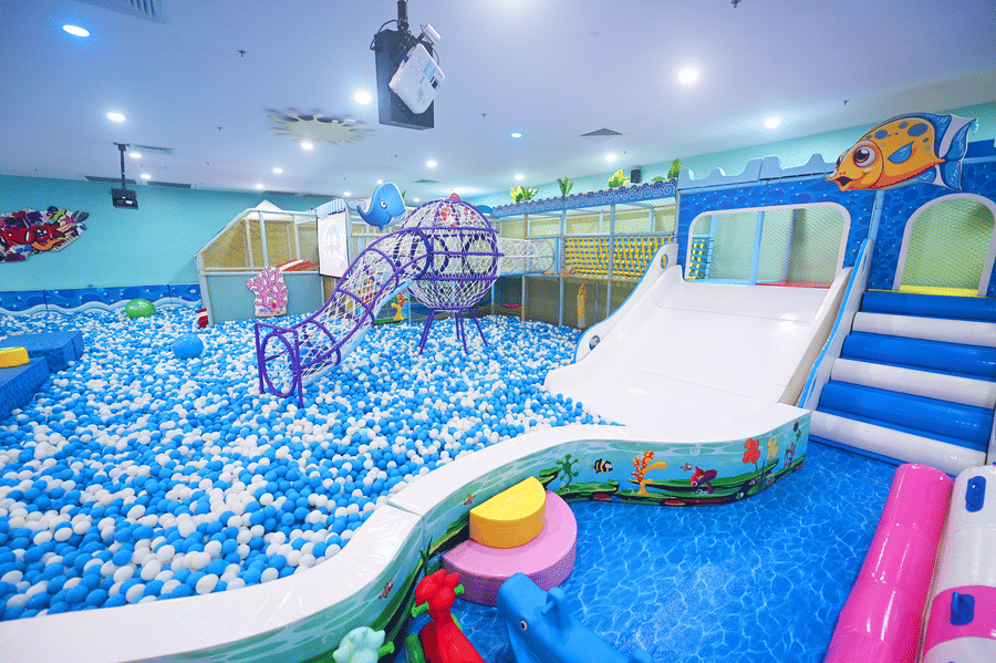 Indoor play area with a large ball pit, slides, and various play structures under bright lights.