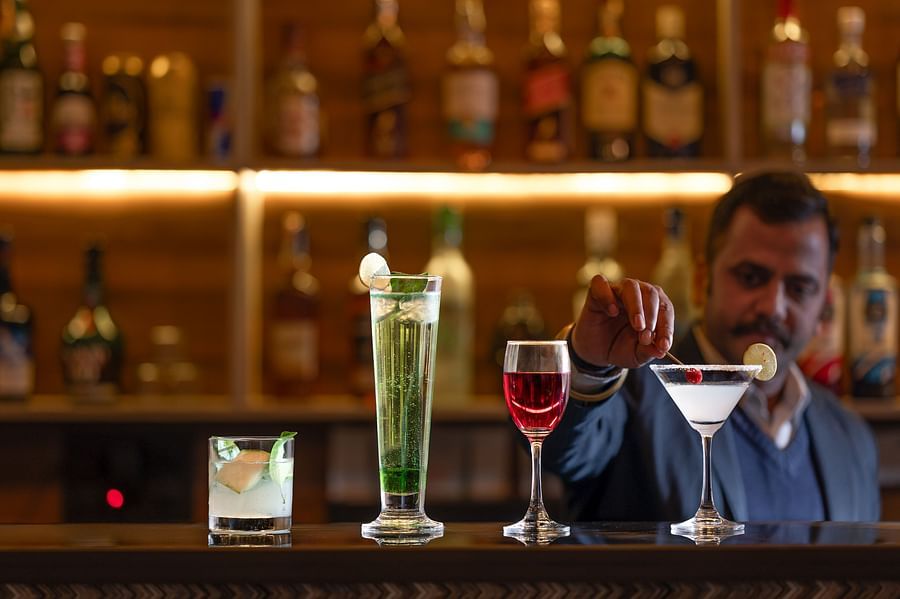 A well-lit hotel bar featuring a selection of bottles and drinks, with a bartender serving them - Clarks Inn Express, Near Jammu Bari Brahmana Railway Station