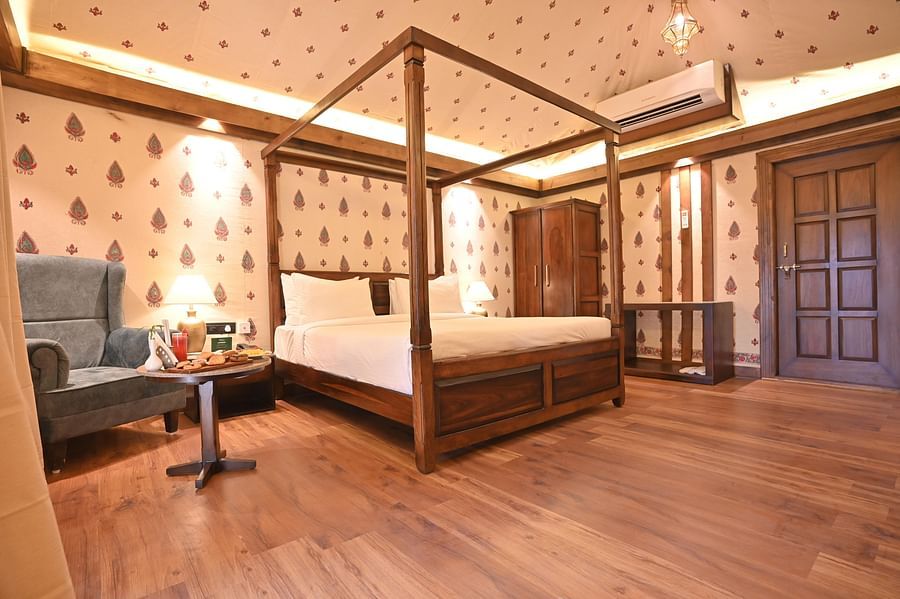 A Premium Tent featuring a poster bed, air conditioner, wardrobe, bedside table with lamp, and a sofa chair with centre table where food items are kept - The Baagh Ananta Elite, Ranthambore