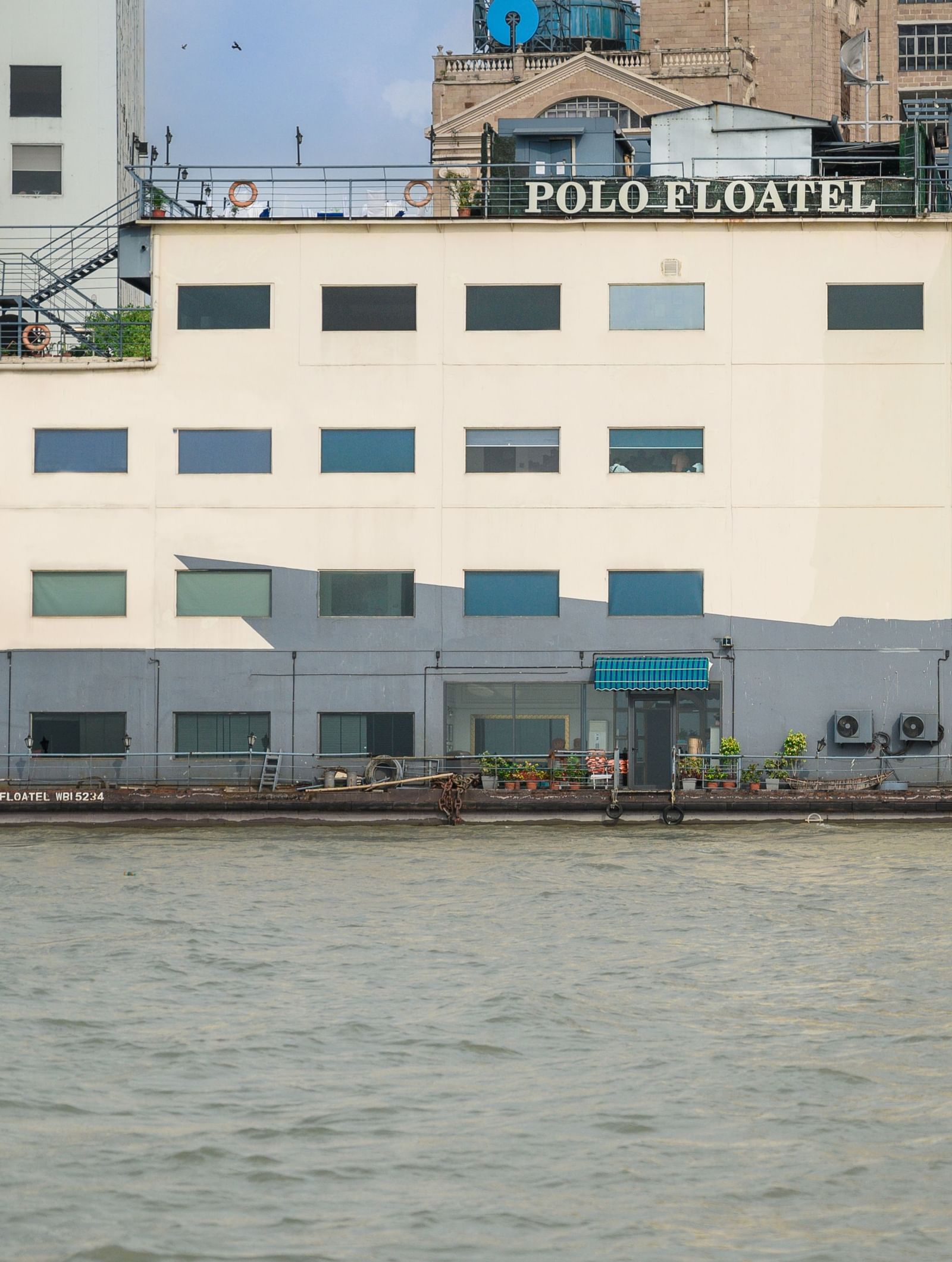 An exterior view of the Polo Floatel Kolkata, a multi-storey, white building with large windows, floating on the Hooghly River.