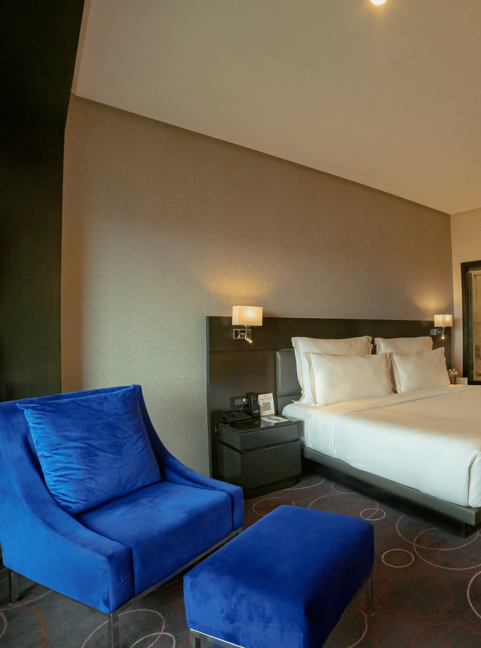 Hotel room featuring a double bed and a blue lounge chair with a leg rest – Narayani Heights Hotel & Resorts